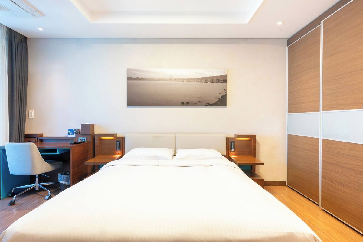 Habitación de hotel con una cama grande, un escritorio con silla, un armario de madera y un cuadro en la pared.