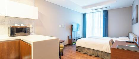 Una habitación de hotel con kitchenette, cama, escritorio y televisor.