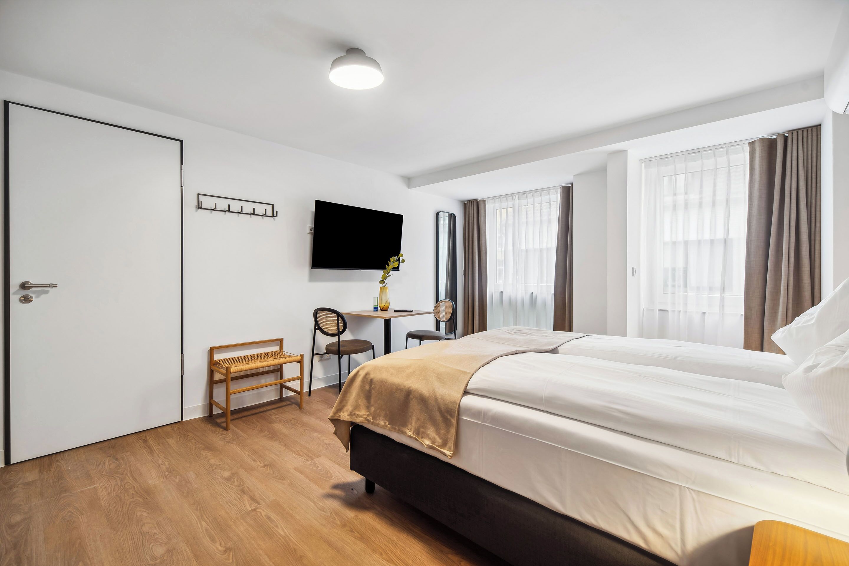 A hotel room with a bed, a desk, a chair, a TV, and a coat rack.