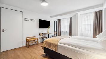 A hotel room with a bed, a desk, a chair, a TV, and a coat rack.