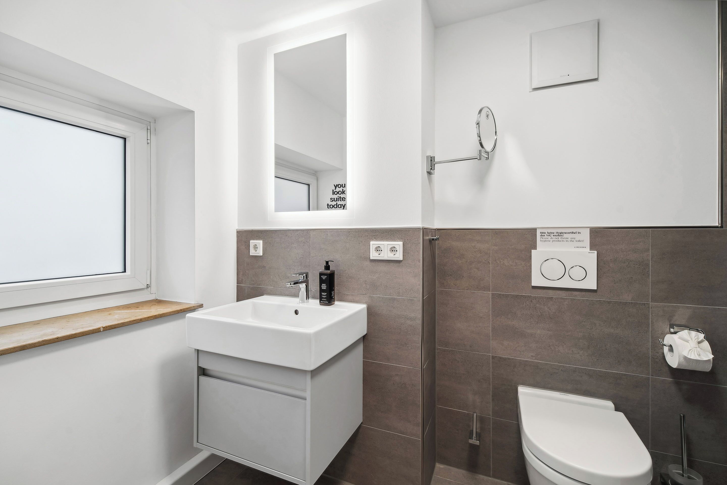 Une salle de bain moderne avec un lavabo blanc, un miroir et des toilettes.