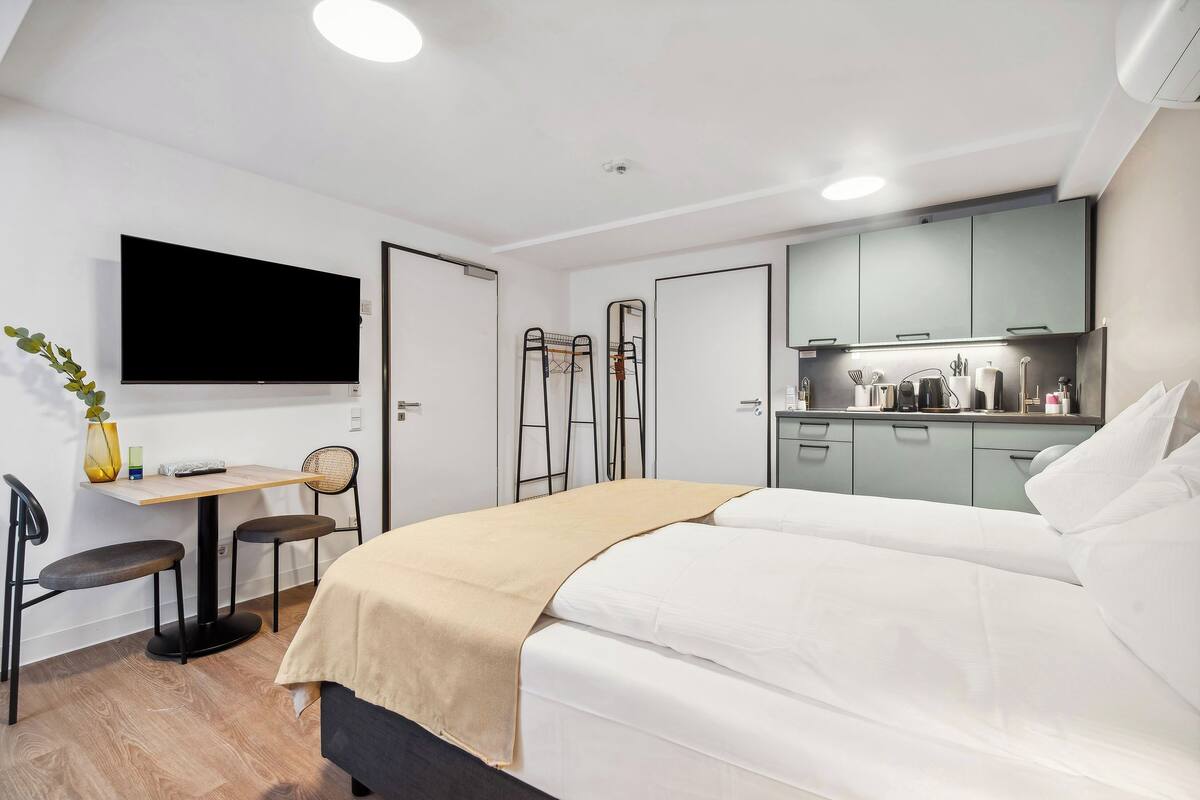 Une chambre d’hôtel moderne équipée d’un lit, d’un bureau avec une chaise, d’une télévision et d’une kitchenette.