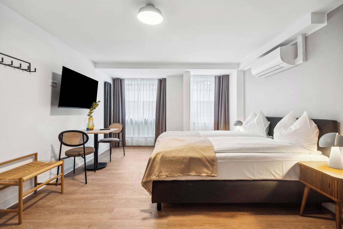 Une chambre d’hôtel moderne dotée d’un grand lit, d’un téléviseur fixé au mur, d’un bureau avec une chaise et d’une fenêtre avec des rideaux.