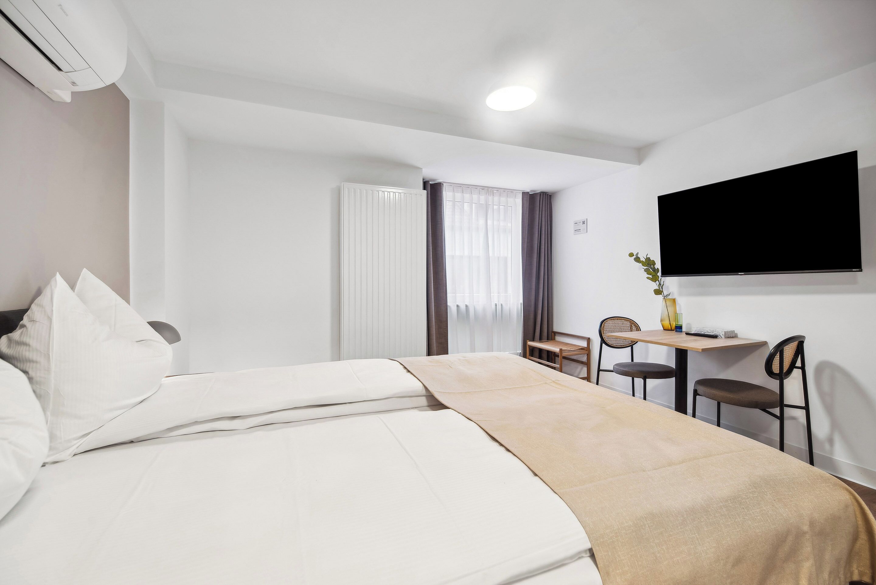 A hotel room with a bed, a desk, two chairs, a TV, and a window with curtains.