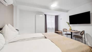 A hotel room with a bed, a desk, two chairs, a TV, and a window with curtains.