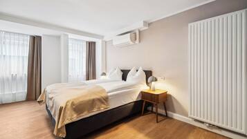 Una habitación de hotel moderna con una cama grande, lámparas de noche, un radiador y una ventana con cortinas.