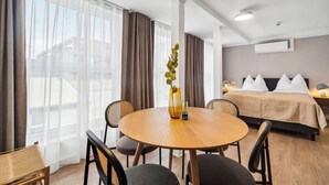 A hotel room with a round wooden table, two chairs, a bed with white pillows, and a large window with sheer curtains. - Limehome Kassel Wilhelmsstraße (Kassel)