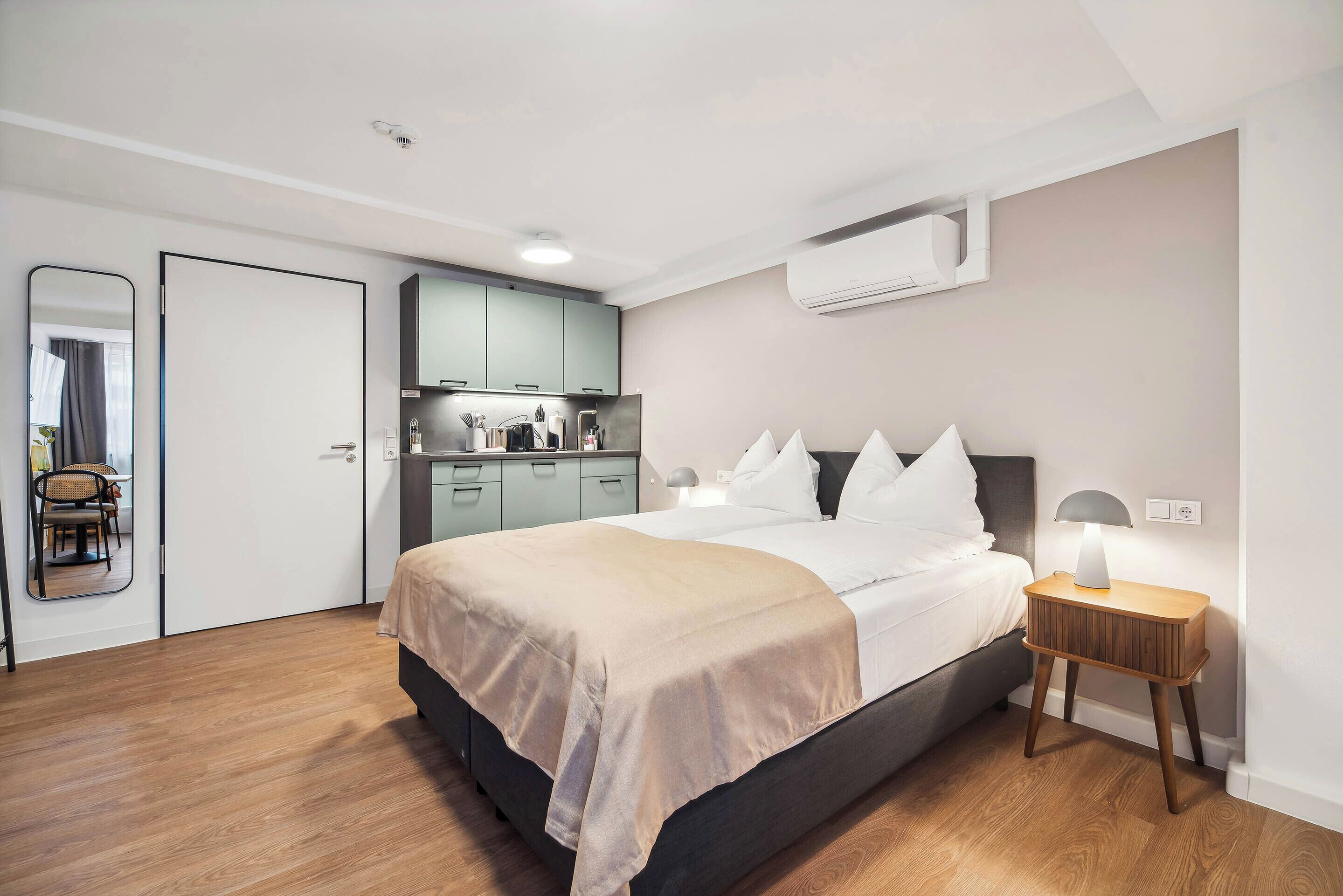 A bedroom with a bed, bedside table, and a small kitchenette.