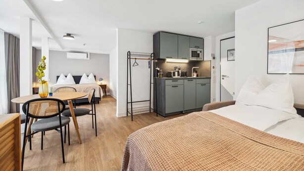 A hotel room with a bed, a dining area with a table and chairs, a kitchenette, and a bathroom. - Limehome Kassel Wilhelmsstraße (Kassel)