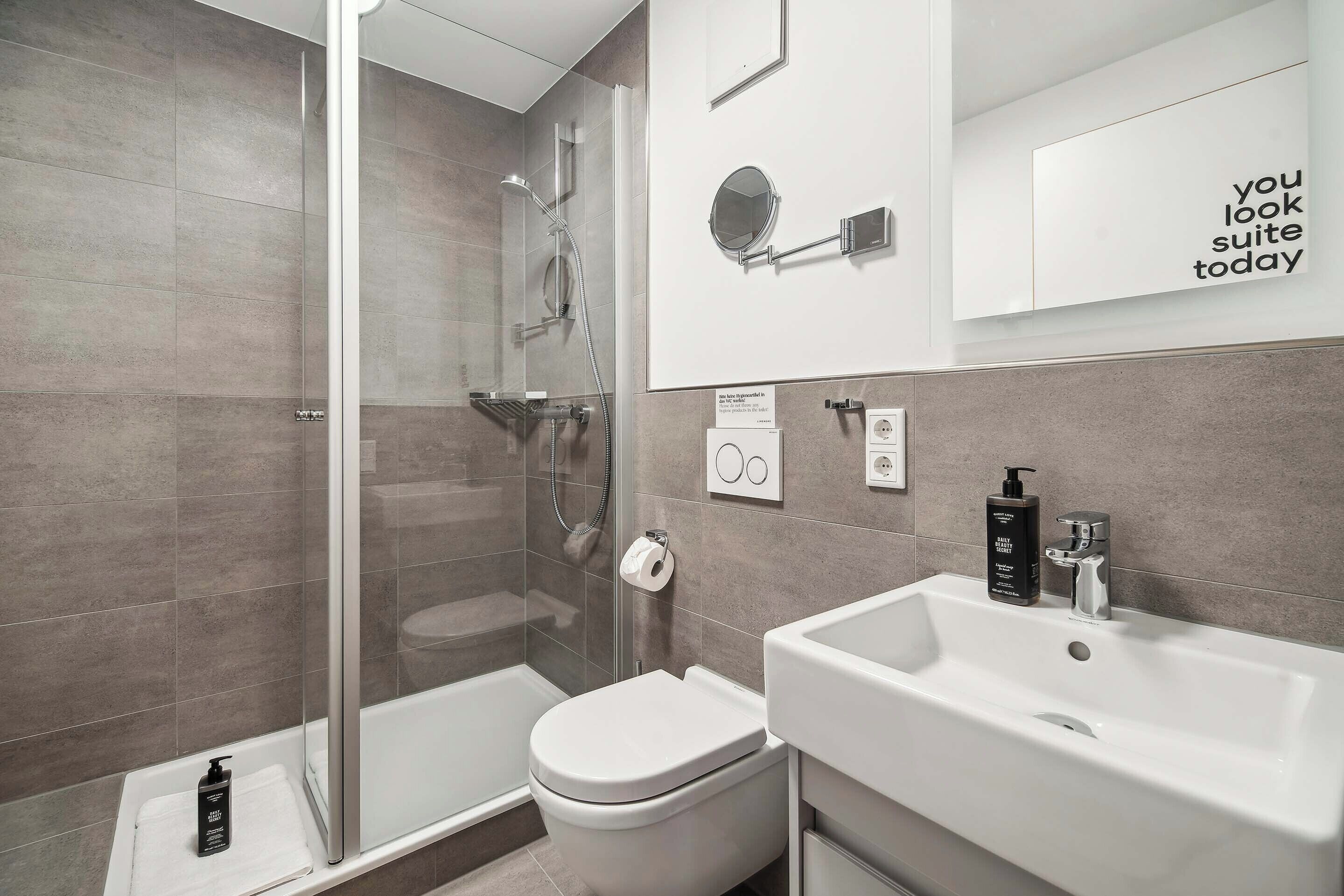 A modern bathroom with a glass shower enclosure, a white sink, and a toilet.