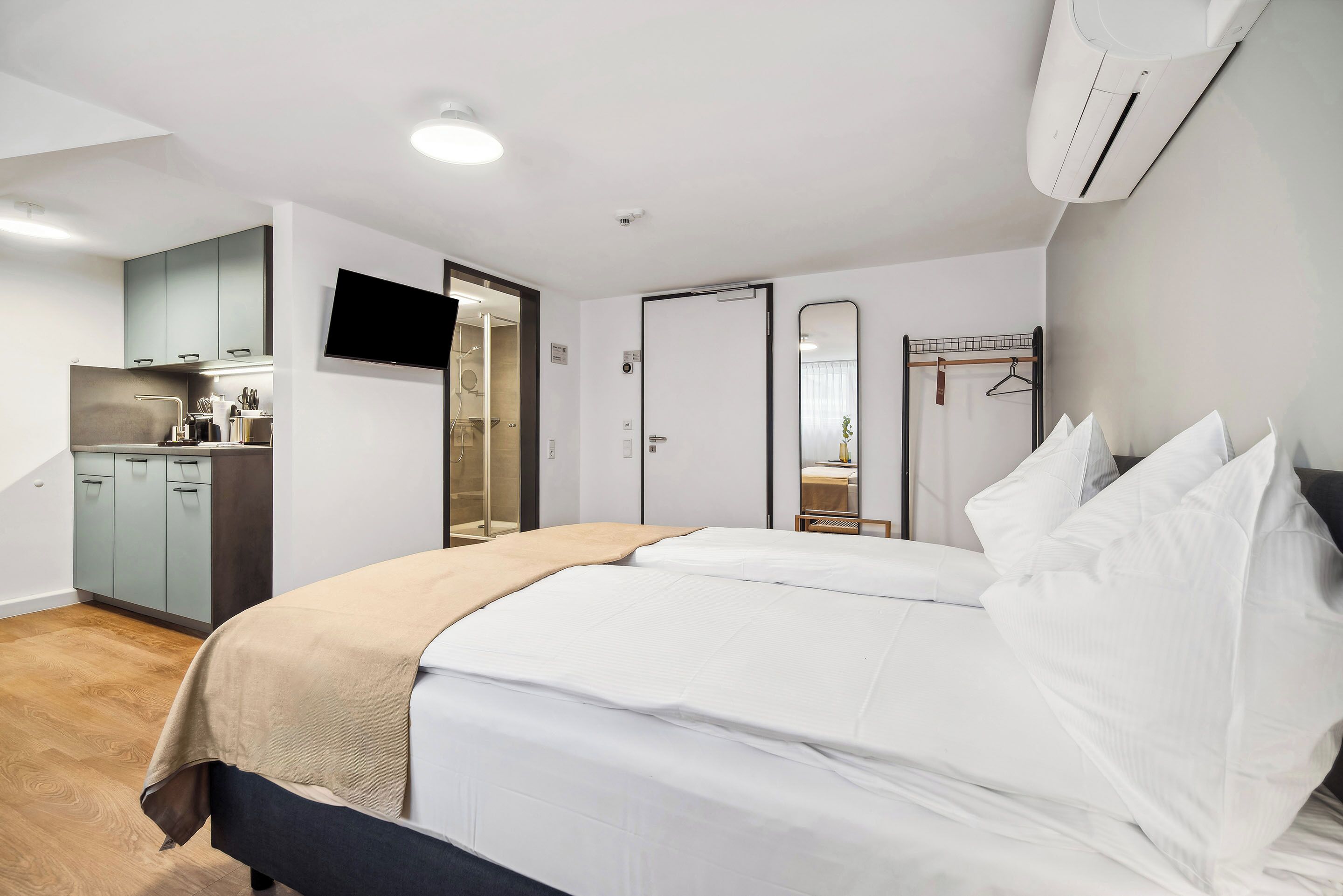 A modern hotel room with a bed, a TV, a wardrobe, and a kitchenette.