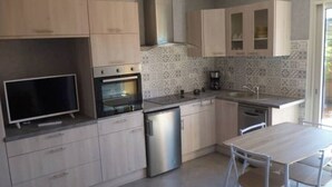 Eine moderne Küche mit hellen Holzschränken, einem Einbauofen, einem Kühlschrank, einer Kaffeemaschine und einem Essbereich mit Tisch und Stühlen.