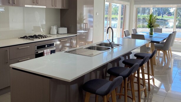 A modern kitchen with a large island, bar stools, and a dining area with a view. - Modern waterfront luxury escape near Shepparton (Mooroopna)