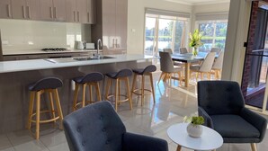 A modern kitchen with a central island, bar stools, and a dining area with a table and chairs. - Modern waterfront luxury escape near Shepparton (Mooroopna)