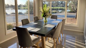 A dining room with a table set for six, large windows, and a view of a lake and park. - Modern waterfront luxury escape near Shepparton (Mooroopna)