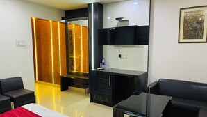 A modern hotel room with a bed, two black sofas, a small table, a TV, and a decorative wall piece. - Hotel Royal Galaxy (Kanpur)