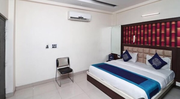 A hotel room with a bed, a chair, an air conditioning unit, and a decorative headboard. - Hotel Royal Galaxy (Kanpur)