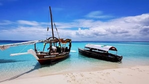 Two boats anchored near a sandy beach with clear turquoise water and a blue sky. - Tsunami village  (Bwejuu)