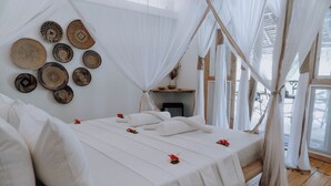 A room with a bed, white bedding, a canopy, and wall-mounted woven baskets. - Tsunami village  (Bwejuu)