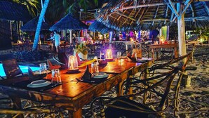 A beachside restaurant with wooden tables, thatched umbrellas, and a pool. - Tsunami village  (Bwejuu)