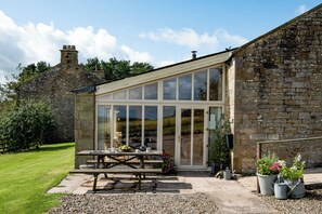 A stone building with a glass conservatory, a picnic table, and potted plants.