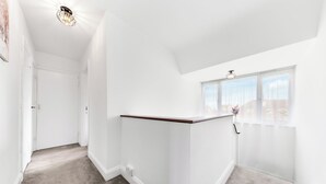 A narrow hallway with a white wall, a wooden trim, and a window with a view of buildings. - Amazing 3-bed Flat in Golders Green Near Station (London)