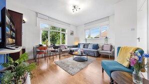 A spacious living room with a sofa, armchairs, a coffee table, and a TV. - Amazing 3-bed Flat in Golders Green Near Station (London)