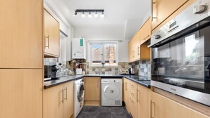 A modern kitchen with wooden cabinets, a built-in washing machine, and a stainless steel oven. - Amazing 3-bed Flat in Golders Green Near Station (London)