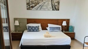Une chambre à coucher comprenant un lit, une tête de lit, des tables de chevet, une lampe, un tableau et un ventilateur de plafond.