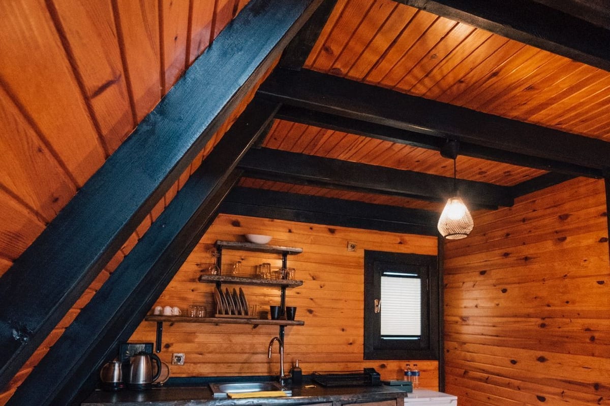 Ein rustikales Blockhaus im Inneren, mit Holzausbau, einer Küchenzeile inklusive Spüle und Schränken sowie einem Fenster mit Jalousien.