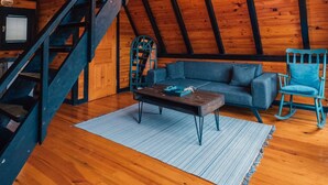 A loft-style room with exposed wooden beams, a blue sofa, a wooden coffee table, and a staircase with a blue railing. - Sapanca Saklı Bungalov (Sapanca)