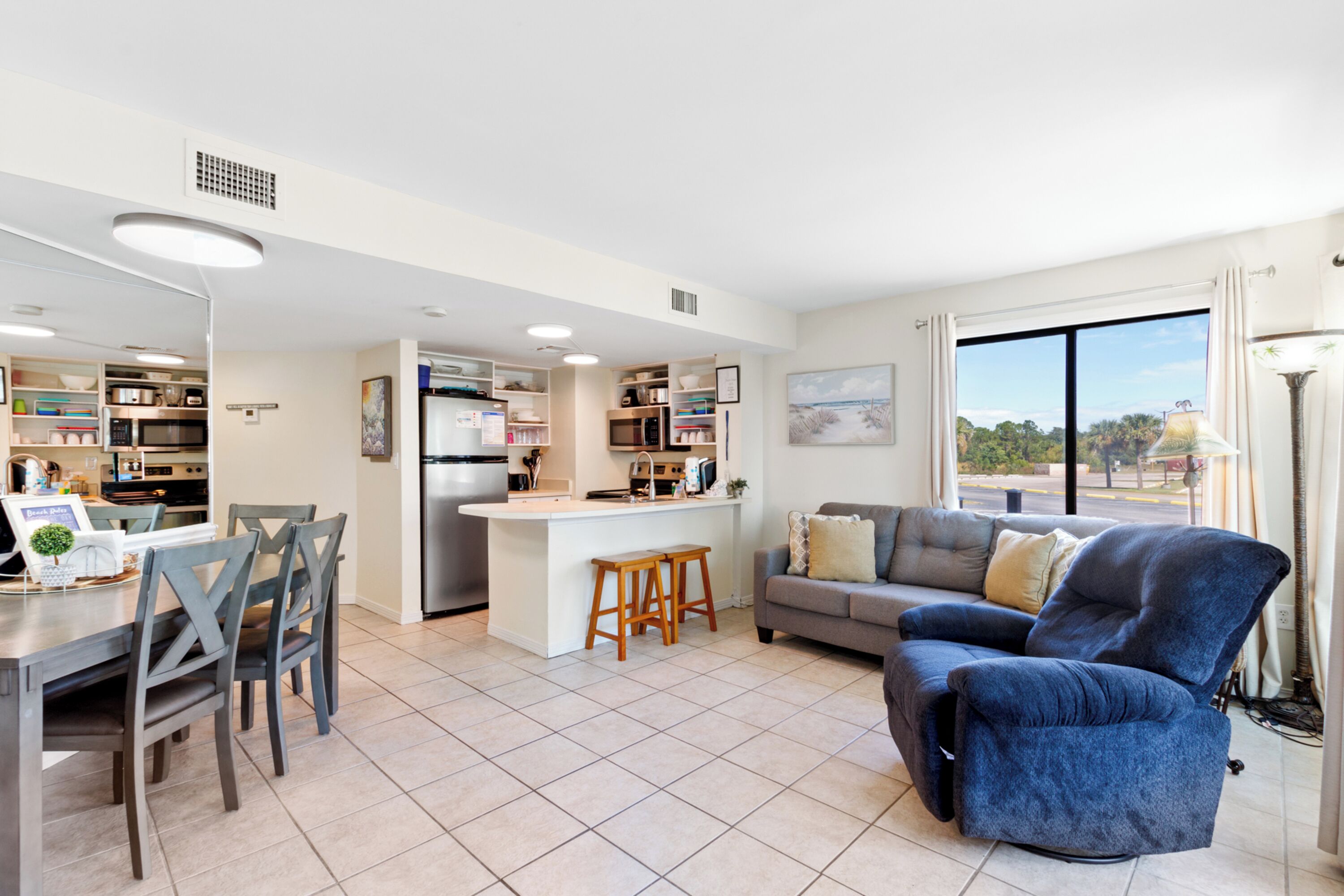 A modern kitchen with built-in appliances, a dining area with a table and chairs, a sofa, and a large window offering a view.