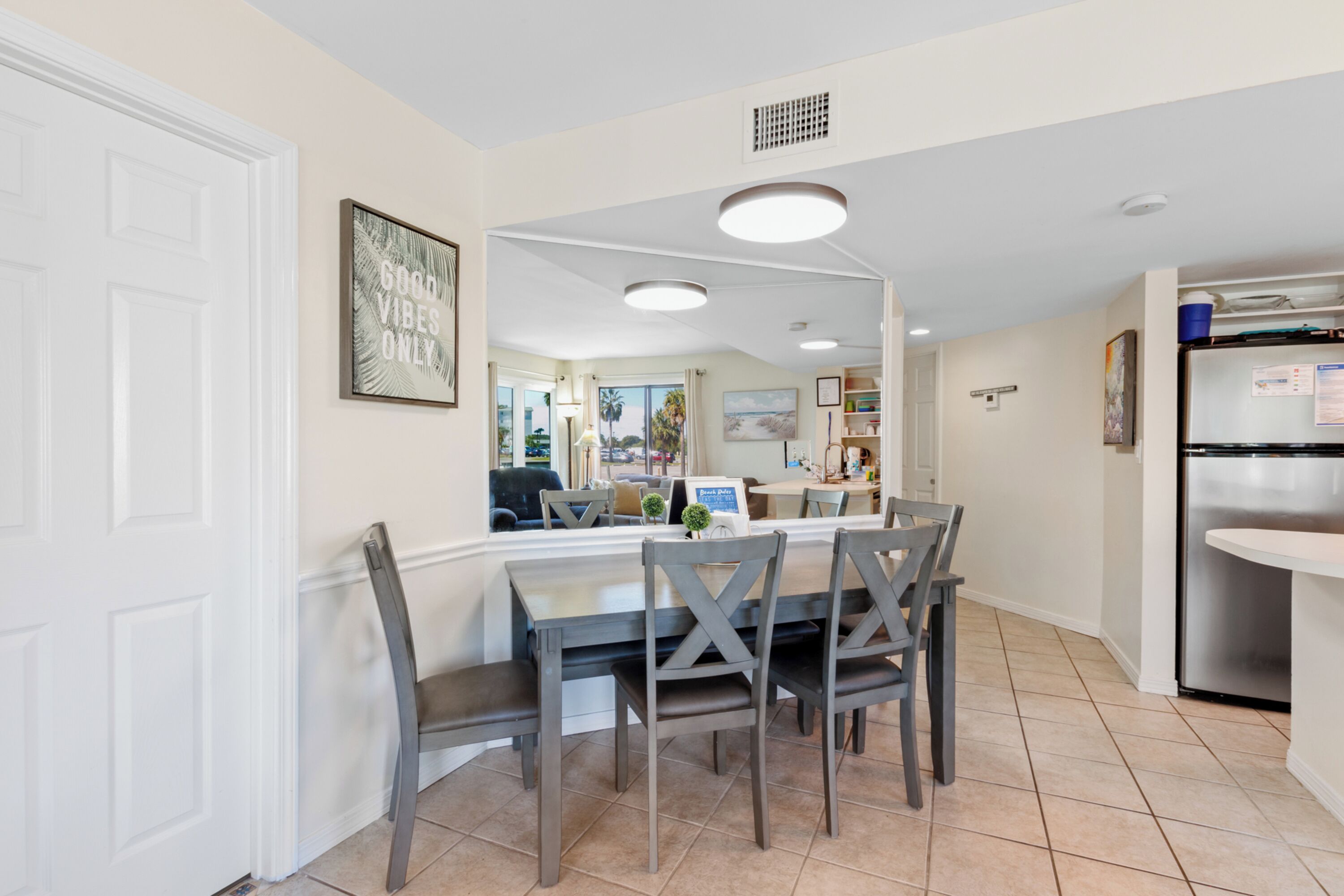 A modern kitchen with a dining area, featuring a white door, a framed picture on the wall, and a stainless steel refrigerator.