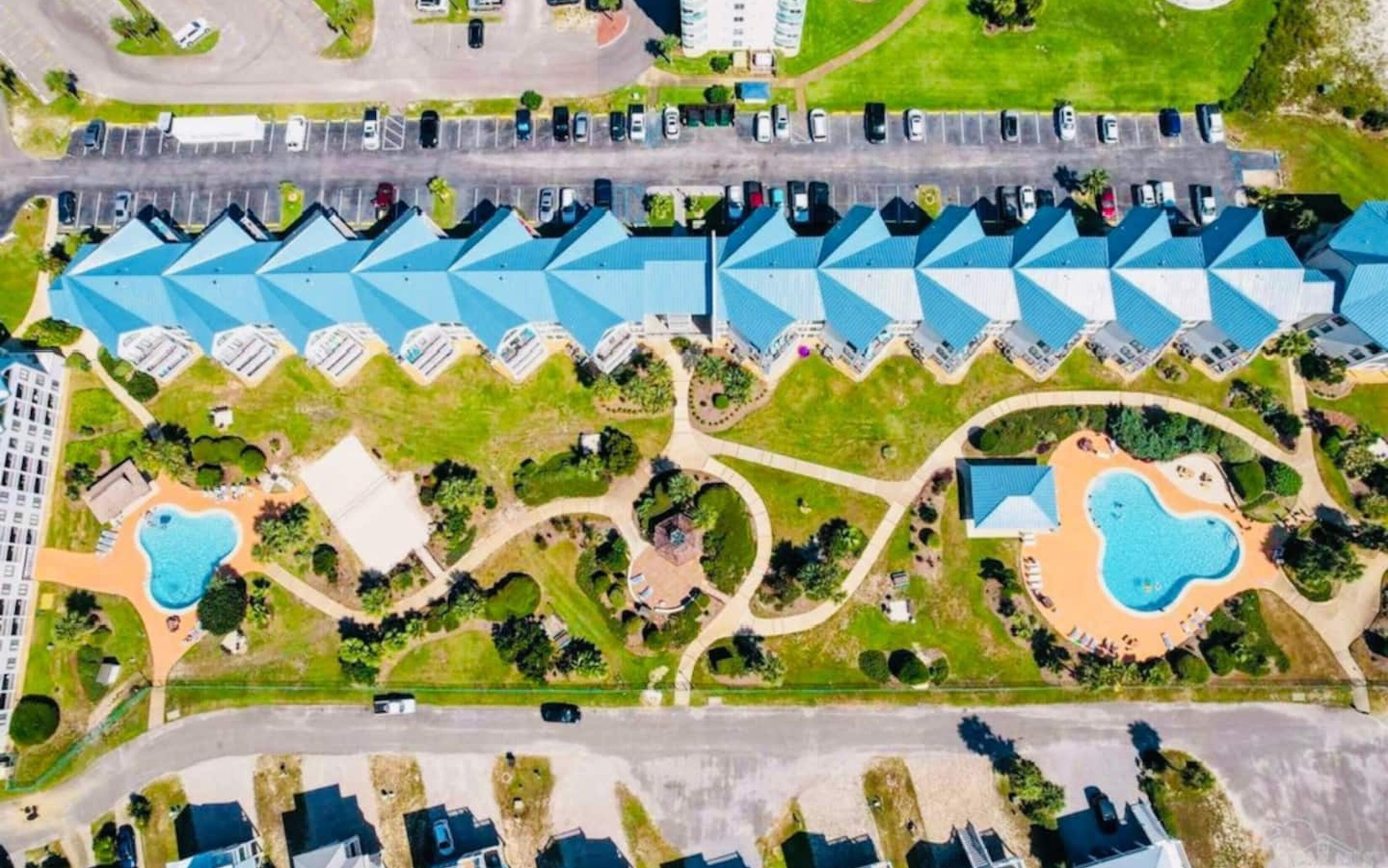 Vue aérienne d’un complexe hôtelier comprenant plusieurs bâtiments aux toits bleus, une piscine centrale et des espaces paysagers aménagés.