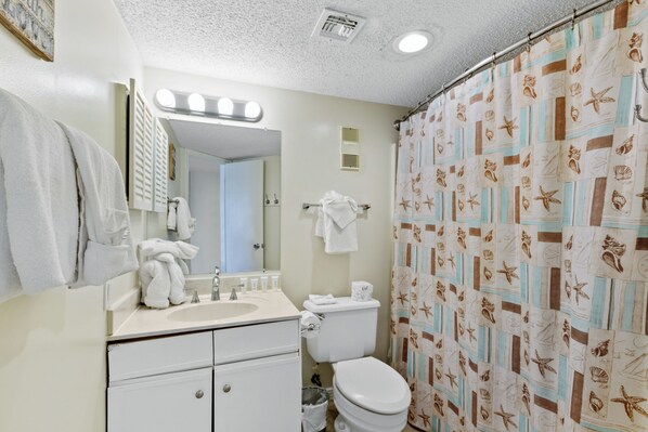 A bathroom with a sink, mirror, toilet, and shower curtain with a nautical pattern.