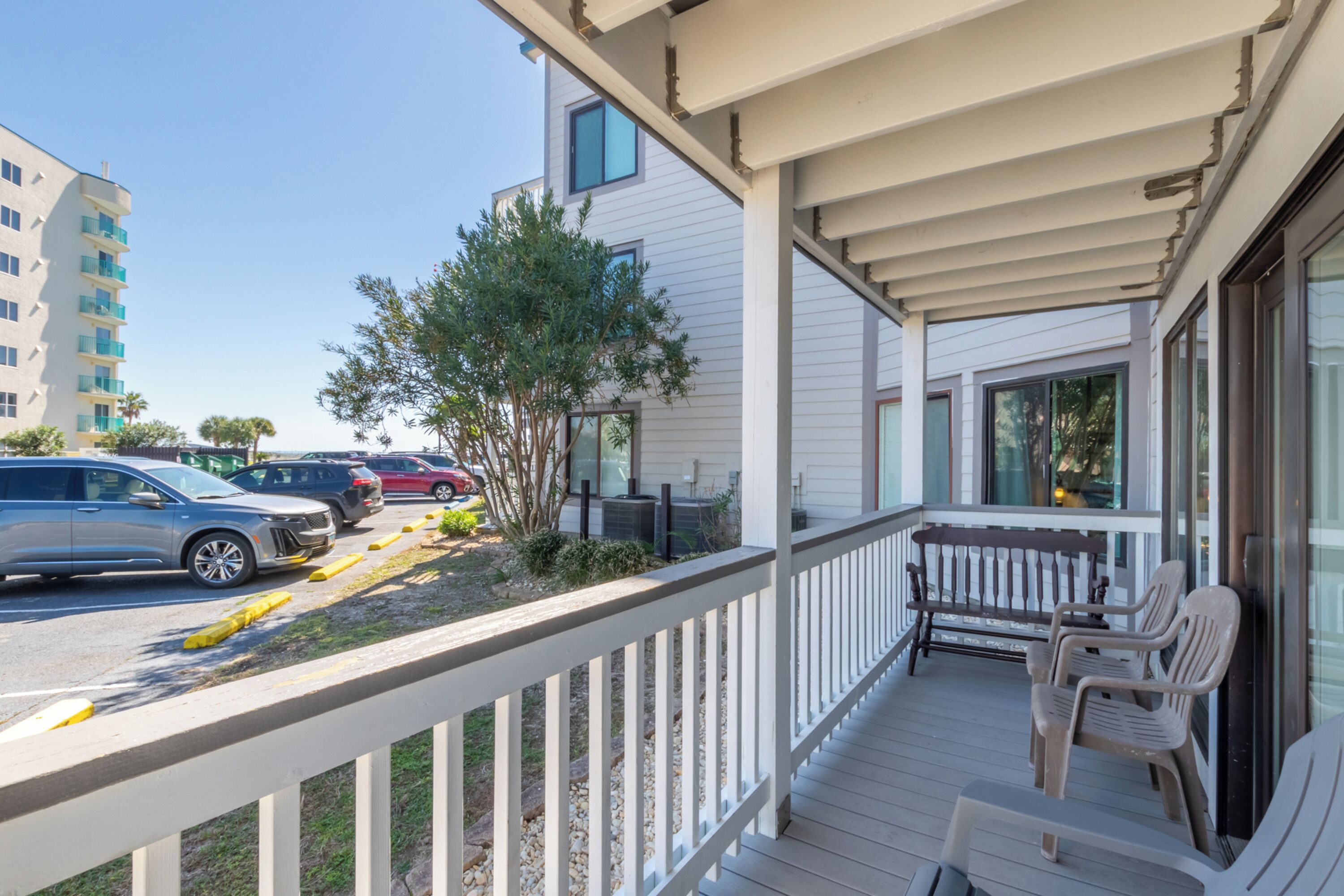 A wooden deck with outdoor seating, a view of parked cars, and a building in the background.