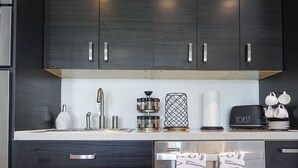 A modern kitchen with dark cabinets, stainless steel appliances, and a coffee maker.