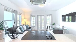 A modern kitchen with a central island, a dining area with a glass table, and a living space with a sofa and curtains.
