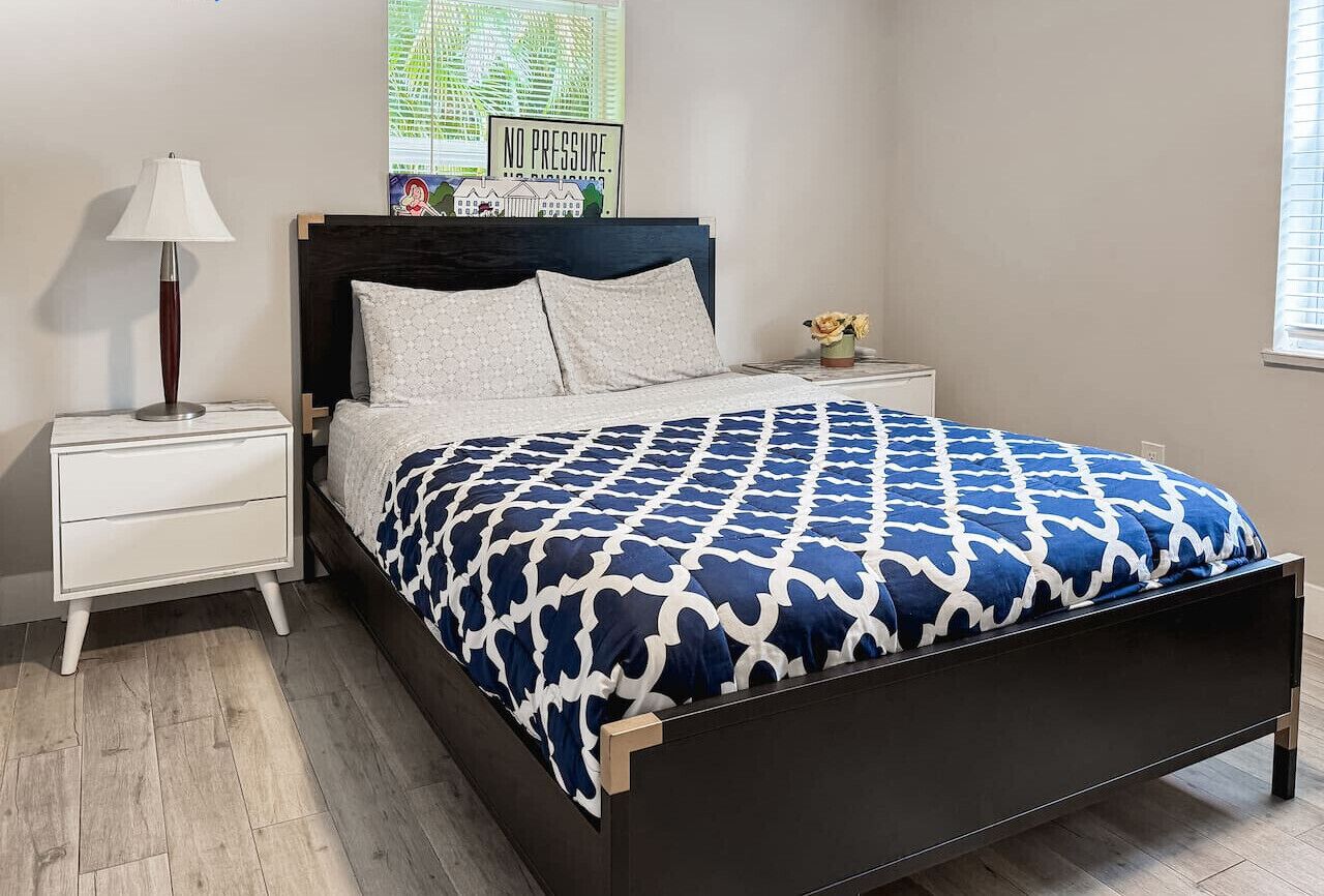A bedroom with a bed, a nightstand, a lamp, and a wall decoration.