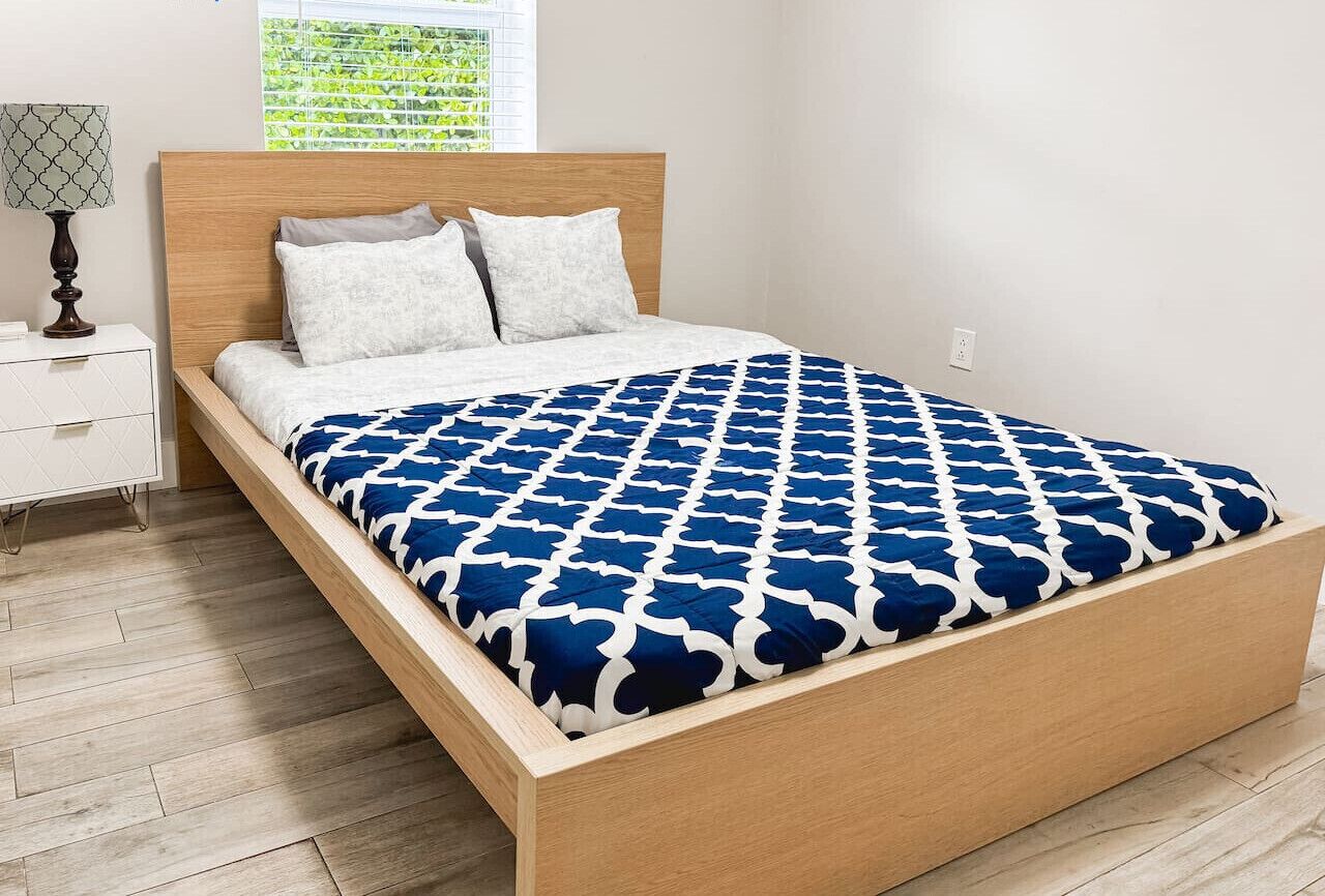 A bed with a wooden frame, white bedding, and a blue patterned bedspread.