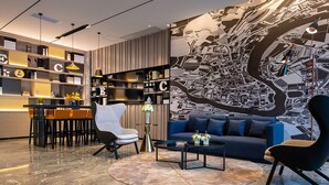 Una sala moderna con un sofá azul, un sillón blanco y un comedor con mesa y sillas. Se observa un mural grande en la pared y una estantería con adornos.