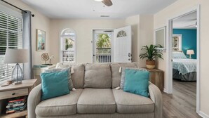 A living room with a beige sofa, a ceiling fan, a window with blinds, and a door leading to another room. - 'A Shore Thing' - Pool - North Myrtle Beach! (North Myrtle Beach)