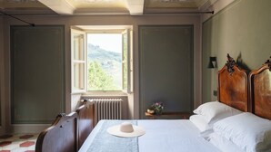 A bedroom with a large bed, a wooden headboard, a radiator, a window with a view of greenery, and a chair. - Luxury Langhe Pool Vigne Di Fagnano (Santo Stefano Belbo)