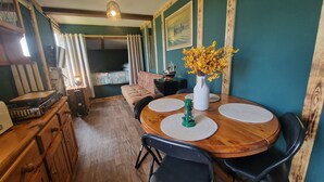 A cozy dining area with a wooden table, chairs, and a vase with yellow flowers. - Sea View hut Sleeps 4/6 (Holyhead)