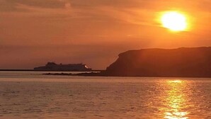 A sunset over a calm sea with a ship in the distance and a cliff on the right. - Sea View hut Sleeps 4/6 (Holyhead)