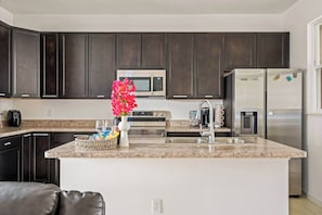 Una cocina con armarios oscuros, un microondas, un refrigerador, una encimera de granito, una cafetera y un florero con flores.