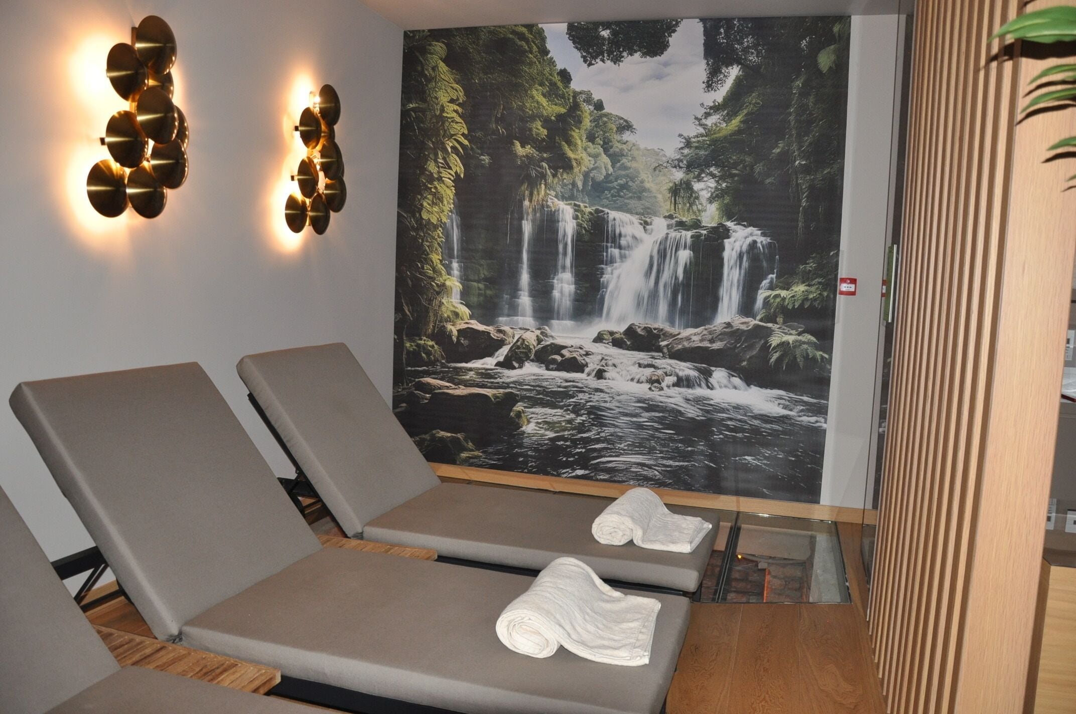 Et spa-rum med to liggestole, et stort vandfaldsmaleri og vægmonterede lamper.