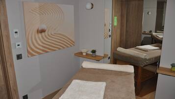 Un moderno cuarto de spa con una camilla de masaje, un cuadro abstracto grande y un estante de madera con una planta pequeña.