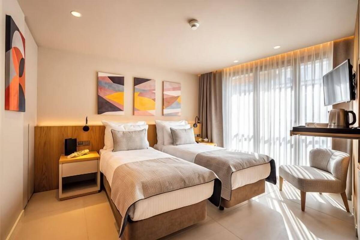 A hotel room with two beds, a desk, a chair, and a TV.
