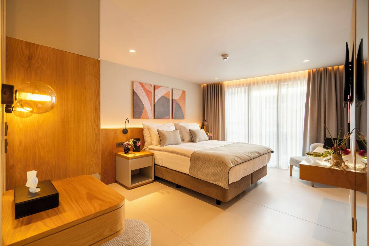 A modern hotel room with a large bed, bedside tables, a desk, and a TV mounted on the wall.